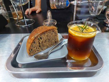 Limon suyuyla karıştırılmış kahve bardağında dilimlenmiş limon. Muzlu pastanın yanında biberiye yaprakları var. Dükkanda limonla karıştırılmış kahve ferahlatıcıdır.