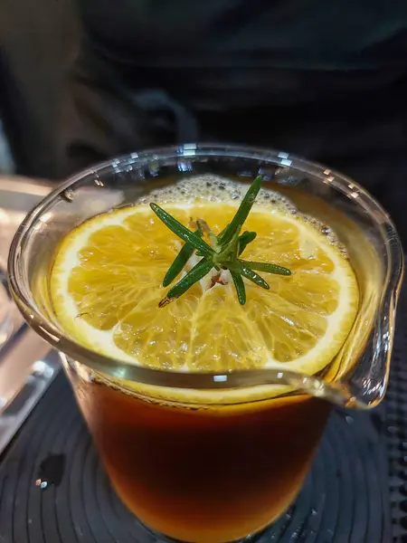 Sliced lemon in a coffee mug mixed with lemon juice. There are rosemary leaves on top. Coffee mixed with lemon in the shop is refreshing