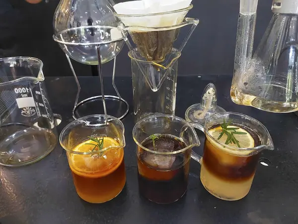Sliced lemon in a coffee mug mixed with lemon juice. There are rosemary leaves on the top three mugs. The background is a drip coffee mug. and clear glass test tubes. Coffee mixed