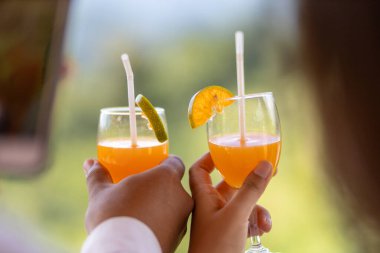 Erkekler ve kadınların ellerinde taze sıkılmış portakal suyu bardaklarını tıkırdatarak bir bardağa yerleştirilmiş taze mandalina suyu.