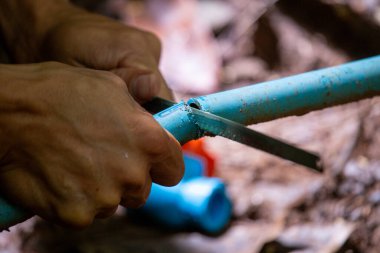 Seçici odak noktası mavi PVC su borusu. Plastik su borusunu kesmek için küçük bir testere kullanmış. Su sistemini PVC borularından onarmak için.