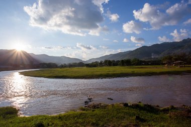 Manzara, nehir, dağlar, yeşil çimenler, gün batımı, parlak gökyüzü.