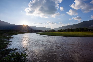 Manzara, nehir, dağlar, yeşil çimenler, gün batımı, parlak gökyüzü.