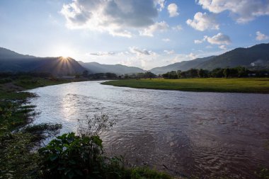 Manzara, nehir, dağlar, yeşil çimenler, gün batımı, parlak gökyüzü.
