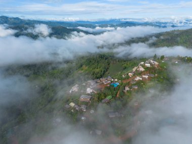 Yüksek açılı bir manzara, dağların ortasında beyaz sisle çevrili bir köy. Güzel manzaralar, ormanların ortasındaki köyler, yeşil dağlar, açık gökyüzü. Bir İHA 'dan fotoğraflar