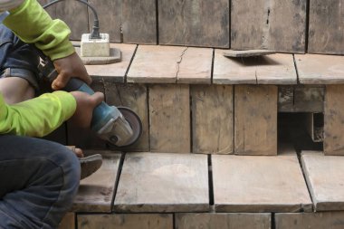 Seçici odak. Teknisyenin elindeki öğütücü, ahşap tahtayı ve ahşap merdivenleri cilalamak için öğütücü kullanıyor. Şekli güzelleştirmek için..