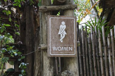 Beyazla yazılmış kadınlar tuvaleti için seçici tahta tabela. Ormanın derinliklerinde bir kafe tuvaleti. Gölgeli, doğal bir şekilde dekore edilmiş..