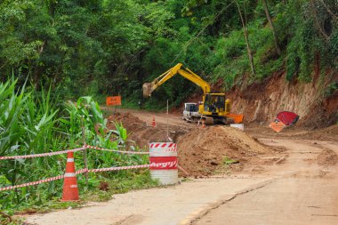 Bir kepçe yağmur mevsiminde toprak kayması sonucu zarar gören bir ormanın kırsal kesiminde çalışıyor. Tayland 'da kırsal bir yol onarılıyor.