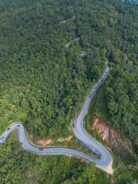 Yolun yüksek açılı görüntüsü her iki taraftan ormanı kesiyor. Dikey Dönen Dağ Yolu. İnsansız hava aracıyla yüksek açılı yeşil bir orman..