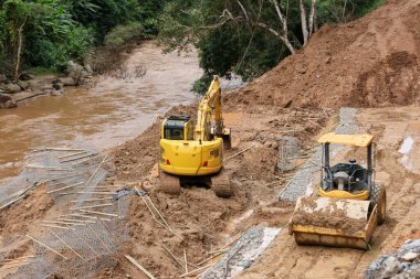 Kırsal yolun manzarası bir yol müteahhiti tarafından bir kepçe tarafından onarılıyor. Yol, yağmur mevsiminde nehir boyunca uzanan heyelan boyunca ormanın içinden geçiyor..