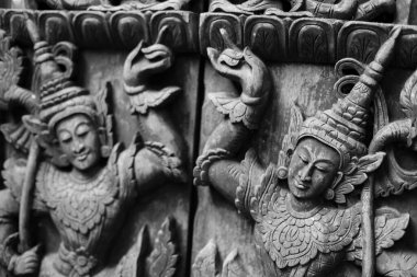 Black and white image. A carved wooden door with Thai deity motifs is commonly found in Thai temples.