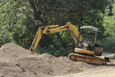 Kum yığınının üzerindeki sarı çapa, doğal orman arka planı, ormandaki yol yapım alanı..