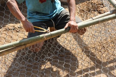 Seçici odak: Yolu engellemek için bir kaya bariyeri oluşturmak için ağın etrafına sarılmış çelik tel. Bambu sepetin etrafına sarılmış. Yol inşaatçıları ağlara taş koymak için tel örüyorlar..