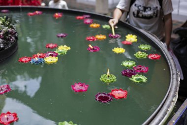 İnsanlar neşeli bir şekilde yüzen mumları yansıtıcı su havuzuna yerleştirirler.