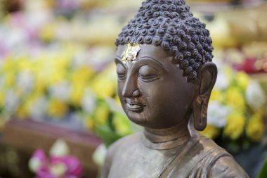 Bronz Buda heykeli, dingin bir ifadeyle, huzuru ve ruhsal huzuru simgeliyor. Hassas altın yaprak alnını süslüyor. Canlı çiçeklerin arasında duruyor, sükunet yaratıyor.