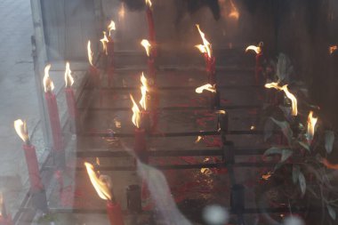 Yanan kırmızı mumlardan çıkan çoklu canlı alevler geleneksel kültürel tören sırasında sıcak ve ruhani atmosfer yaratır. Yumuşak parıltı kutsal mekanı aydınlatır, huzur ve hürmeti yansıtır.