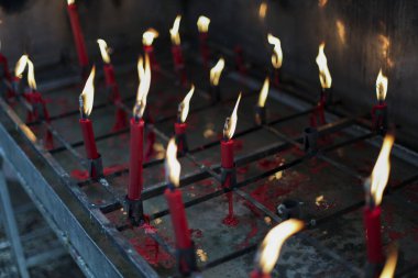 Kırmızı yanan mumlar kutsal tapınağı aydınlatır, huzur dolu ruhsal atmosfer yaratır. Alevler sıcacık bir ışıkla parlıyor, bağlılığı, ibadeti ve kalıcı geleneği temsil ediyor. Sakin bir sahne