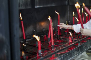 Kırmızı mum yakarak derin bir bağlılık gösteriyor. Titreyen alev, kutsal tapınağın içini aydınlatır. Ayin bir adağı temsil eder, sessiz dua güçlü inancı ve eski geleneği temsil eder.