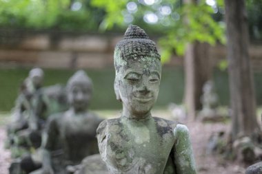 Serene Stone Buddha heykeli yıpranmış, antik tarihi ve ruhsal huzuru çağrıştırıyor. Yosun kaplı heykel, açık bir tapınak bahçesinde sakin ve düşünceli bir duyguyu ifade eder.