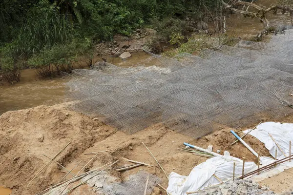 Nehir kıyısı toprak dengelenmesi için kum üzerindeki tel örgüyle zemin hazırlığı