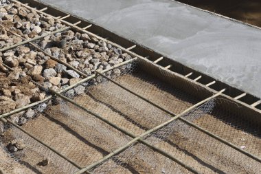 Yeryüzü üzerinde katmanlı çakıl ve sağlam tel örgü takviyesi içeren titiz bir inşaat alanı hazırlığı. Bitişik beton yüzey inşaat ilerlemesi gösteriyor, çalışkan çalışma dayanıklılığına işaret ediyor