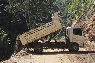 Güçlü bir çöp kamyonu, engebeli dağ yolu, temel yapı. Ağır ekipmanlar, uzak doğal orman ortamı, toprak ve çakıl taşıma. güçlü araç, zorlu gelişim için hayati önem taşıyor