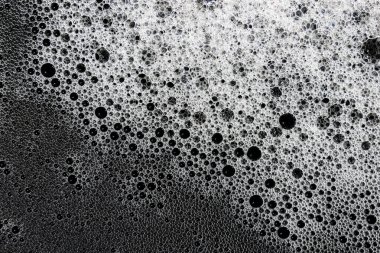 Dinamik yakın plan çok sayıda beyaz kabarcığın derin, karanlık arka plana karşı köpüklü, zengin bir doku oluşturduğunu gösteriyor. Hassas küreler hoş coşkulu desenler sergiliyor. Tazelik hissi uyandırıyor.