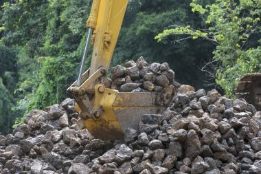 Güçlü kazıcı özenle yer yerinden oynatan, hareket eden kaya yığını yapar. Makine, inşaat alanında endüstriyel gücü gösteriyor. Taş ve molozları etkili bir şekilde toplayarak ilerlemeyi simgeliyor.