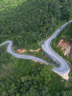 Virajlı yol canlı yeşil ormanın içinden geçiyor. Dağ doğasının etkileyici bir hava manzarası. Zorlu seyahat macerası, uzak ve barışçıl keşifleri teşvik etmek.