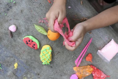 Çocuk neşeli bir şekilde renkli killeri karpuz ve ananas gibi eğlenceli şekillere dönüştürüyor, bu oyunculuk aktivitesinde yaratıcılık ve hayal gücünü ateşliyor.