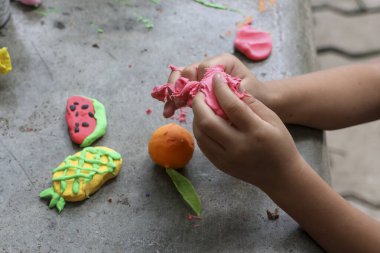 Çocuk elleri neşeli bir şekilde renkli killeri karpuz, ananas ve turuncu gibi meyve formlarına dönüştürür.