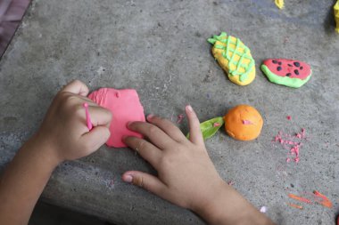 Çocuk elleri mutlu bir şekilde kilden renkli meyve şekilleri yaratıyor, yaratıcılığı ve iyi motor becerileri teşvik ediyor. Bu meşgul edici aktivite neşe ve hayal gücü uyandırır.