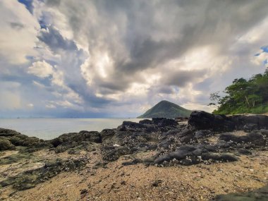 Kayalık sahilde dramatik bulutlu bir gökyüzü ve uzak adayla birlikte sakin bir okyanus. Sahne korku ve sükuneti çağrıştırıyor, bulutlar dinamik bir tavan yaratıyor dingin deniz manzarası ve engebeli kıyı şeridi