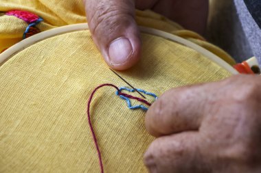 Hassas nakış işlemeye odaklanmış bir el. Geleneksel dikiş sanatı, sarı halkalı kumaşa renkli dikişler ve tutkulu el yapımı yetenekler gösteriyor.