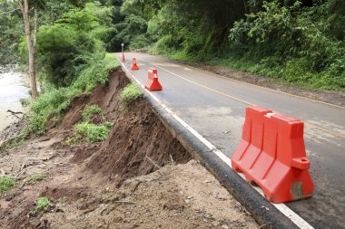 Tehlikeli toprak kayması toprak erozyonunun çöktüğü caddede yol hasarına yol açıyor. Turuncu güvenlik bariyerleri zararlı doğal afetin sonucu olarak tehlike gösteriyor.
