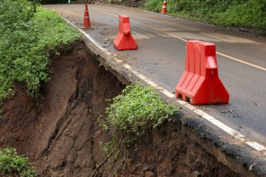 Heyelan yüzünden tehlikeli yol çökmesi. Toprak erozyonu asfalta zarar verdi ve tehlike ve potansiyel risk uyarısı olarak kırmızı güvenlik bariyerleri yerleştirildi