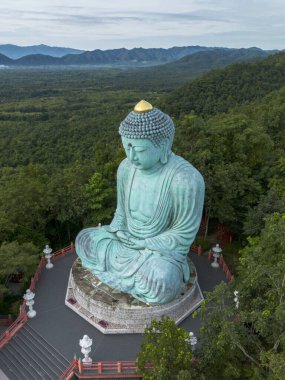 Muhteşem bronz Buda heykeli engin, yemyeşil ormanın ortasında huzur içinde duruyor. Sakin sahne derin dinginlik ve ruhani sükuneti çağrıştırıyor, görkemli dağlar güzel bir zemin oluşturuyor.