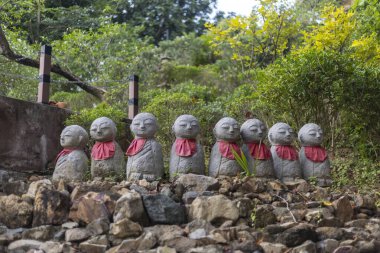 Kırmızı önlük giyen, yeşil yaprakların arasına yerleşmiş, sakin ve sakin bir açık hava manzarası yaratan, sakin ve ruhani atmosferi somutlaştıran, huzur dolu taş heykel sıraları.