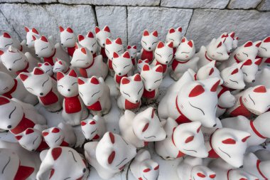 Çok sayıda beyaz seramik tilki heykeli, canlı kırmızı işaretli geleneksel Japon Kitsune figürleri, grup dingin türbesine yakın durun. Her sanatsal heykel antik kültürü ve ruhaniliği yansıtır.