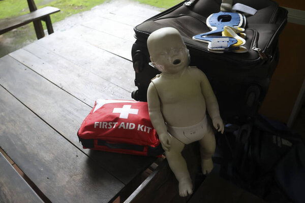 Манекен реанимации младенцев, необходимый для подготовки к реанимации, стоит у красного аптечки. Это мощно передает серьезный характер жизненно важного образования и готовности к чрезвычайным ситуациям, способствуя важнейшему