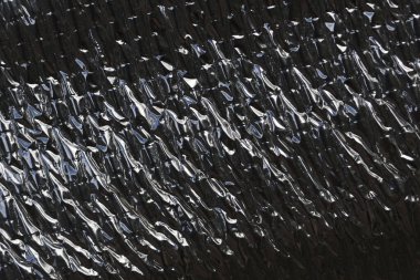 Close up of dark metallic background with crinkled foil texture. This abstract, industrial pattern of heat protection sheet creates rough, reflective surface