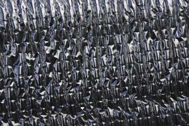 Close up black metallic background texture of crinkled heat protection sheet. dark, shiny, reflective surface creates an abstract pattern for an industrial and modern design