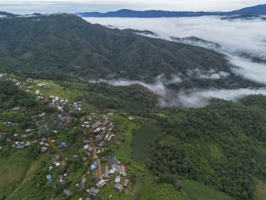 Majestic aerial view of remote village on green mountain slope above peaceful sea of mist. This tranquil landscape captures quiet beauty of hillside community