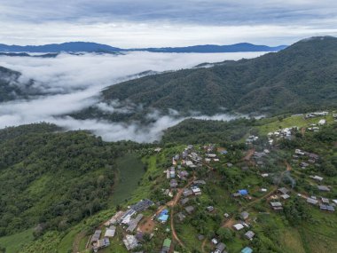 Serene aerial view of remote hill tribe village on mountain with sea of mist. tranquil landscape with green forest and valley under cloudy sky in Asia