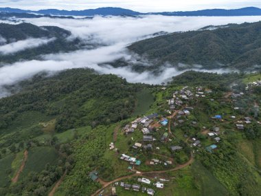 Peaceful aerial view of remote rural village on green mountain top. beautiful morning landscape with sea of fog covering lush valley, evoking serene and calm feeling