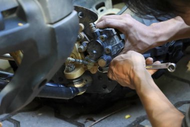 Atölyedeki motor tamiratı ve bakım servisi için odaklanmış mekanik el tutma aracı. Adam garajdaki metal araç parçalarını dikkatle tamir ediyor.