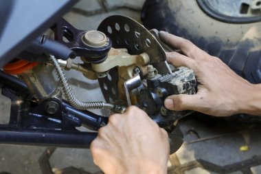 Kirli elle tamirat yapan odaklanmış tamirciyi kapat. Dörtlü bisiklet fren diski, kalibre ve süspansiyon üzerinde araç bakımı yapan adam