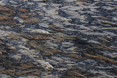 Doğal gri ve kahverengi kaya dokusu arkaplanının yakın görüntüsü. Bu sert taş yüzeyi katı ve toprak karakterli katmanlı jeolojik deseni gösteriyor.