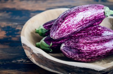 Fresh organic Graffiti eggplants in a wooden bowl on an old wooden table.