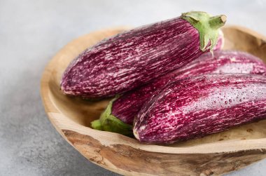 Fresh organic Graffiti eggplants in a wooden bowl on a concrete background.